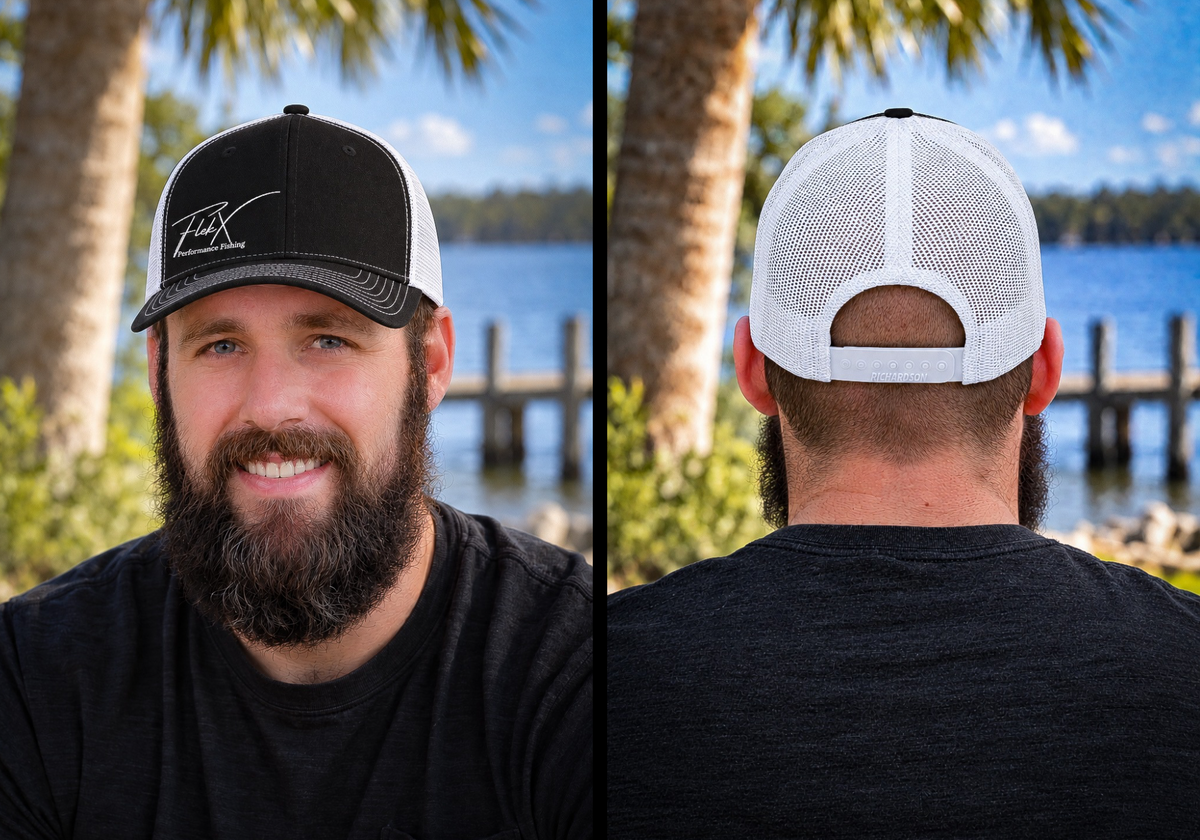 Bearded man in a black t-shirt standing by the water at a palm-lined dock, wearing the black-front FlekX Signature Hat with white script FLEKX embroidery; the rear view shows the white mesh back and adjustable snap closure. A Richardson 112 christian fishing trucker hat - faith based fishing apparel for long days on the water.